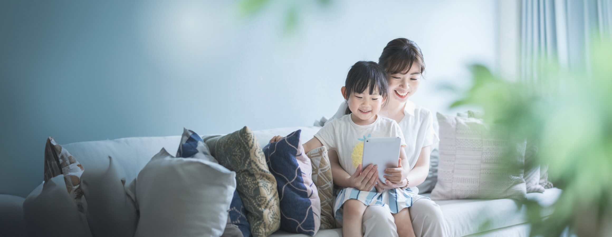 母親と女の子がソファーに座りタブレット端末を見ている画像